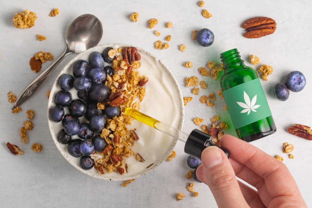 A hand adds cannabis tincture to a bowl of yogurt
