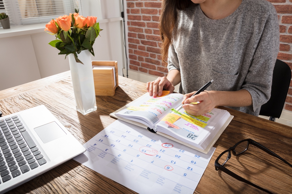 A woman marks her paper calendar while sitting at her desk.