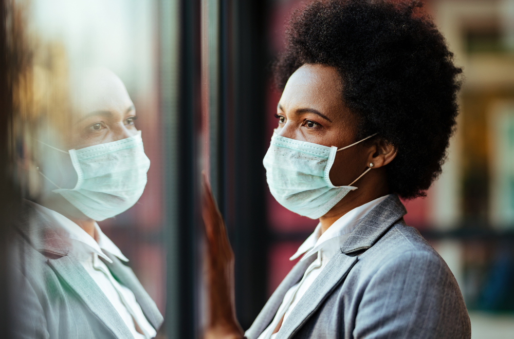 A woman wearing a mask looks through a window while considering diabetes and COVID-19