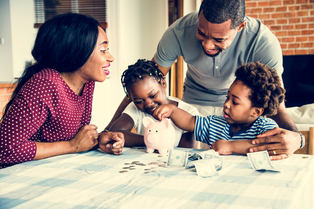 Family sits around a table and puts money in a piggy bank.