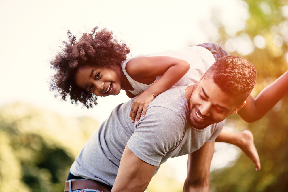 A father carries a young daughter on his back.