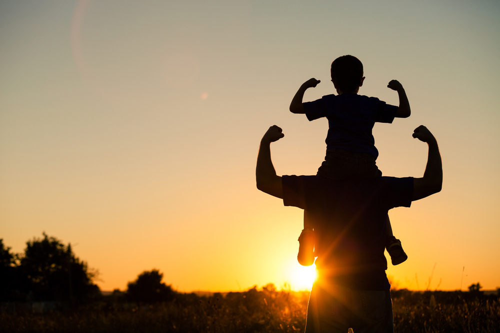 Father and son flexing arms in sunset
