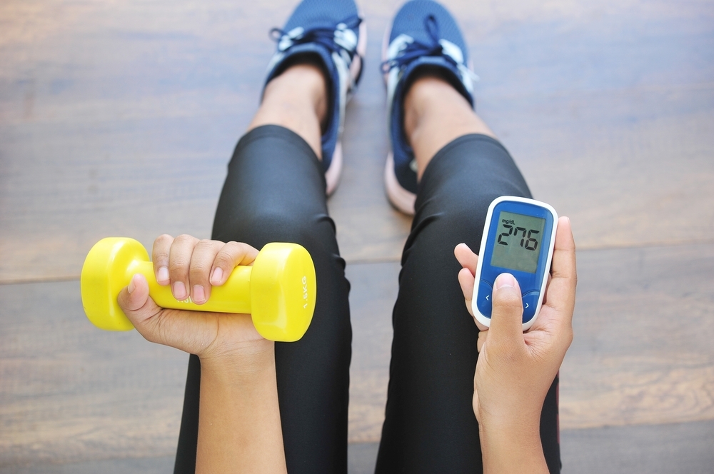 Woman holding dumbbell and glucose monitor.