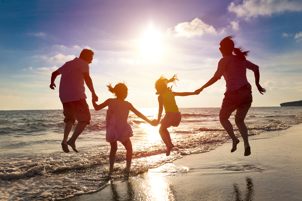 A family holds hands and jumps together on the beach.