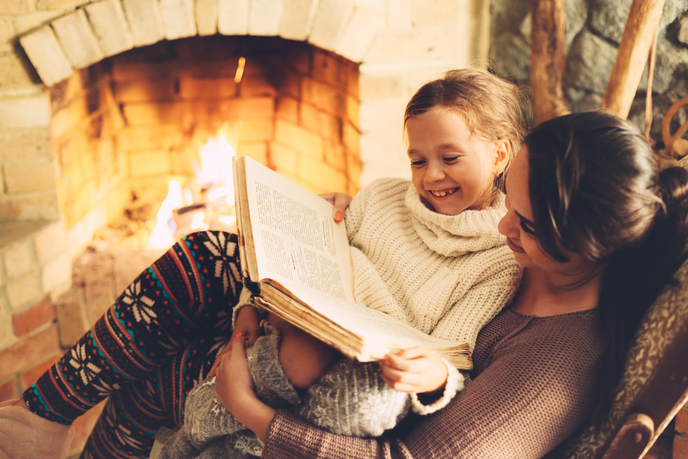 Mother and daughter read a book together in front of a cozy fire