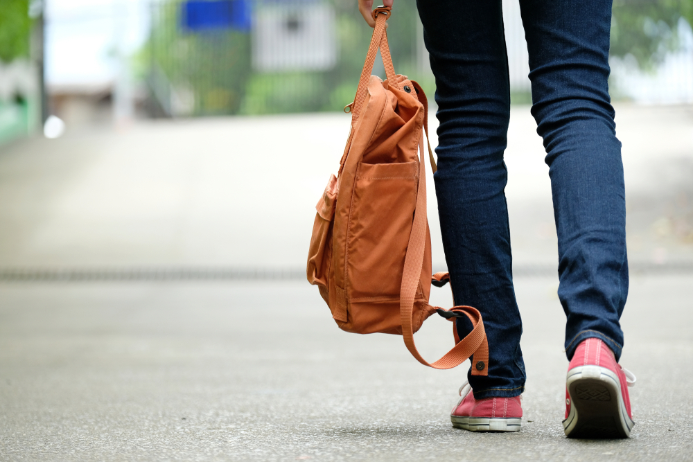 A person walking into a hospital carrying an overnight bag.