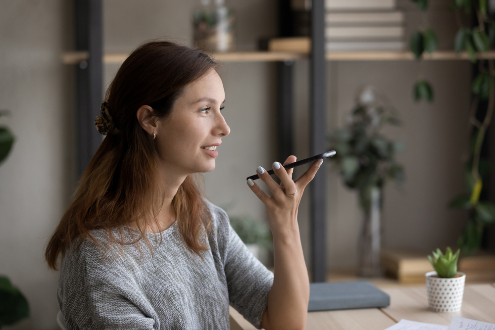 A woman speaks into her mobile phone while sitting at a table.