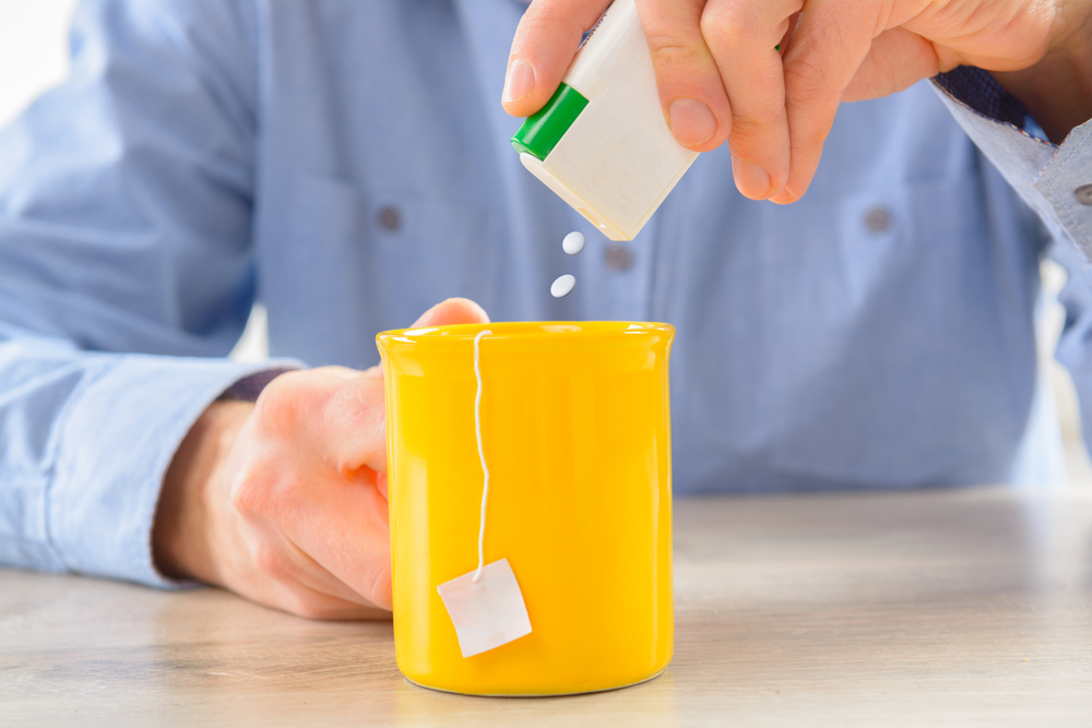 Person adding artificial sweetener to tea