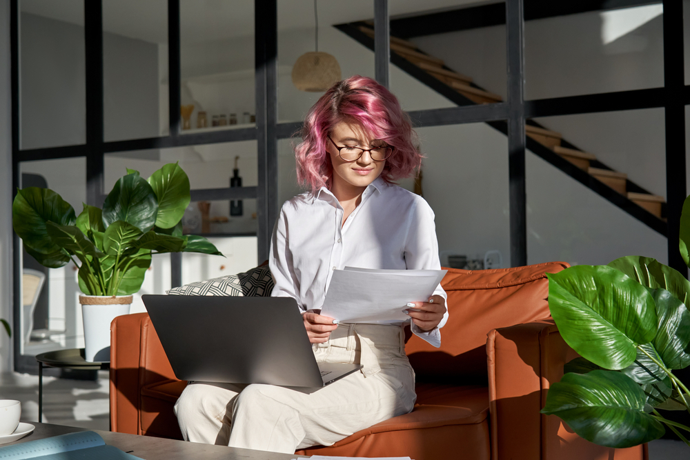 A young woman sits in front of her computer reading a paper.