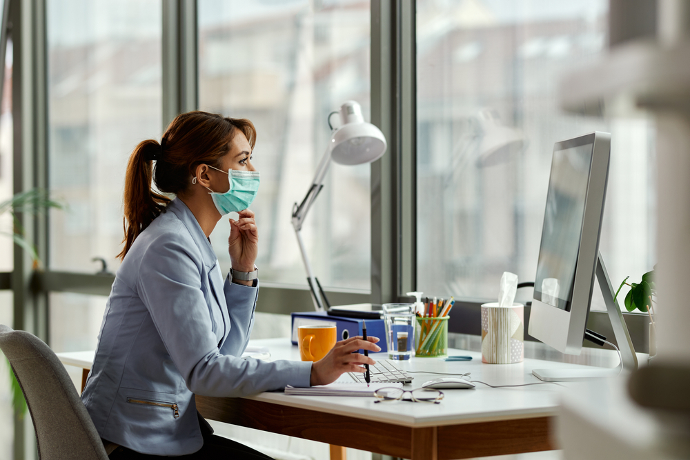 A woman wears a mask at her desk while she works at her computer.