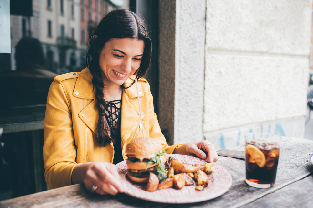 A young woman happily prepares to eat a hamburger meal