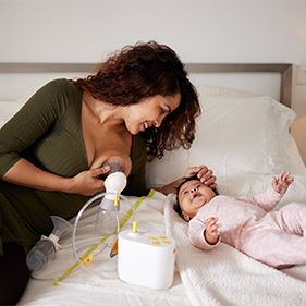 Mother using breast pump she received from Edgepark and smiling at her baby